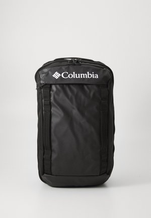 Črn nahrbtnik Columbia z kviltirano teksturo, zgornjim zadrgo, nastavljivimi stranskimi trakovi in izstopajočim belim logotipom na sprednjem delu.