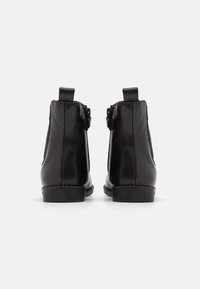 Bottes chevilles en cuir noir avec une texture lisse, un bout arrondi et un talon bas. Dotées de fermetures éclair latérales et de languettes à l'arrière pour faciliter l'enfilage.