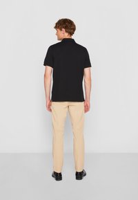 Juoda polo marškinėliai trumpomis rankovėmis, derinami su šviesiai smėlio spalvos kelnėmis. Marškinėliai turi klasikinį kirpimą ir švarų, paprastą dizainą.