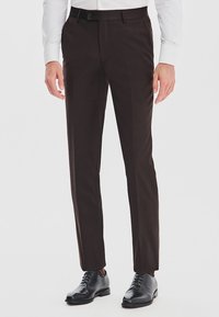 Ciemnobrązowe dopasowane spodnie materiałowe z gładkim przodem, subtelną teksturą i slim fit, w połączeniu z czarnymi skórzanymi butami.
