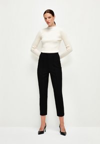 White ribbed long-sleeve top with a high neckline paired with high-waisted black tailored pants and black pointed-toe heels.