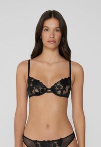 Černá krajková podprsenka s květinovou výšivkou, průhlednými košíčky, podpůrným drátkem a nastavitelnými ramínky, v kombinaci s odpovídajícími průhlednými kalhotkami.