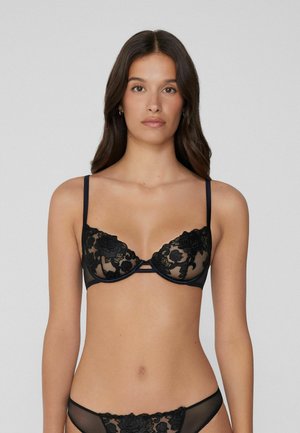 Soutien-gorge en dentelle noire avec broderie florale, coupelles transparentes, soutien-gorge à armatures et bretelles ajustables, associé à un string transparent assorti.
