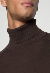 Pull à col roulé marron en tricot doux et texturé, avec une coupe ajustée et un col haut.