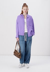 Lavender button-up shirt, white tank top, loose blue jeans, white sneakers, and a brown shoulder bag; relaxed fit; textured fabric.