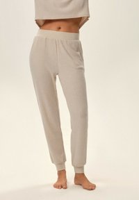 Beżowy zestaw odzieży domowej w prążki, składający się z krótkiego topu i zwężających się spodni. Spodnie mają elastyczny pas oraz miękką, teksturowaną tkaninę.