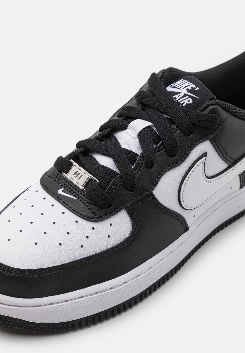 Sneaker Nike Air Force 1 in bianco e nero con tomaia in pelle, punta tonda, perforazioni, lacci neri e dettaglio del logo metallico sulla linguetta.
