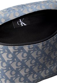 Borsetta in tela con un motivo geometrico blu e beige, chiusura con zip e rivestimento interno nero. Presenta un'etichetta con logo all'interno.