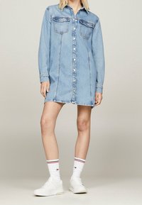 Denim shirt dress, light blue with long sleeves, front buttons, two chest pockets, and a straight silhouette. Paired with white sneakers and striped socks.