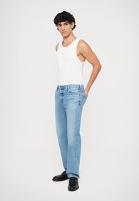 Heledad sinised teksapüksid sirge lõikega, kombineeritud valge triiksärgiga ja mustade kingadega. Kude on pehme tekstuuriga ja minimaalsete kulumismärkidega.