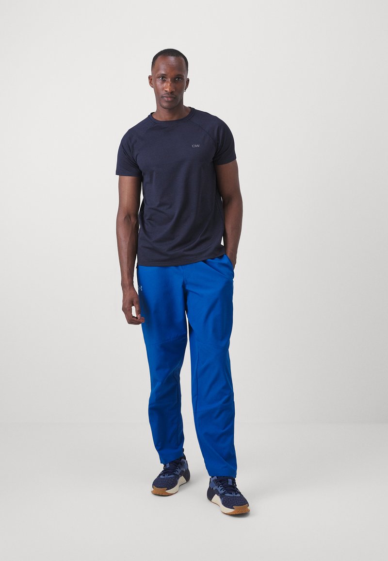 Camiseta atlética de manga corta azul oscuro con escote redondo; combinada con pantalones atléticos azul brillante y zapatillas deportivas oscuras.