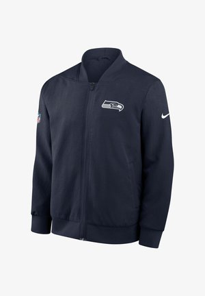 Giacca bomber blu navy in tessuto leggero, con logo Seahawks sul petto e Swoosh Nike sulla manica. Chiusura frontale con cerniera.