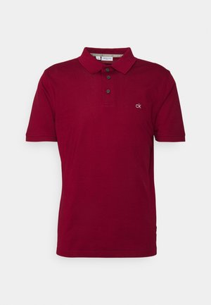Rdeča polo majica iz bombaža z ovratnikom, z zaklepanjem na tri gumbe in majhnim izvezenim logotipom na prsih. Kratki rokavi.