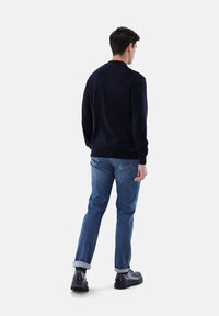 Navy gestrickter Pullover mit gerippten Bündchen und Saum, kombiniert mit hellblauen Jeans, hochgekrempelten Bündchen und schwarzen Lederschuhen.