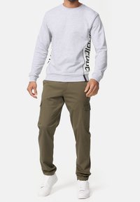 Sudadera gris con branding negro en los laterales, cuello redondo y puños acanalados, combinada con pantalones cargo oliva que tienen bolsillos laterales y un corte relajado.