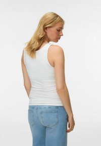 Vit ärmlös topp med en åtsittande design. Mjuk tyg med en slät textur, sedd bakifrån på en person som bär ljusblå jeans.