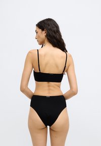 Σετ μαύρο μπικίνι που περιλαμβάνει ένα απλό τοπ με λεπτές τιράντες και ψηλόμεσα εσώρουχα. Κατασκευασμένο από λείο, ελαστικό ύφασμα.