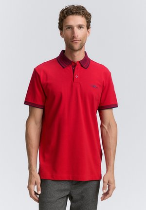 Rød polo-shirt lavet af bomuld, med en kontrastfarvet marineblå krave og ærmekant, samt et lille logo på brystet. Glat tekstur.