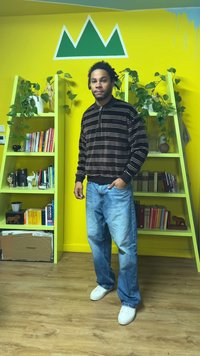 Svart- och vitrandig zip-up-tröja med krage, kombinerad med ljusblå denimjeans och vita sneakers. Gröna hyllor och gul bakgrund.