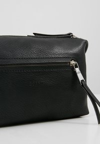 Borsa nera in pelle testurizzata con chiusura a zip, dotata di una zip argentata e di un dettaglio di branding impresso sul davanti.