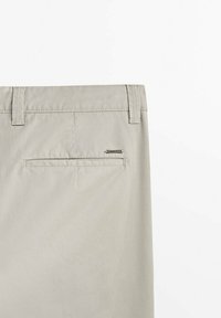 Pantalon beige vu de dos montrant des passants de ceinture et une seule poche passepoilée avec une petite étiquette métallique de marque au-dessus.