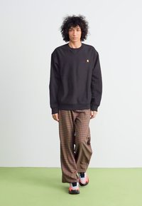 Zwart sweatshirt met ronde hals, gecombineerd met bruine geruite broek. Het model draagt zwart-roze sneakers. Eenvoudige, ontspannen silhouet.