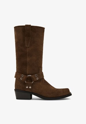Brown suede cowboy boot with a mid-calf height, pointed toe, contrasting black rubber sole, and an adjustable strap with metal accents.
