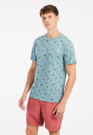 T-shirt vert menthe à manches courtes avec une poche, arborant un motif graphique répété et un tissu doux et texturé. Associé à un short corail.