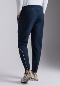 Navy joggers with an elastic waistband, side pockets, and white piping details. Paired with gray and yellow athletic shoes.