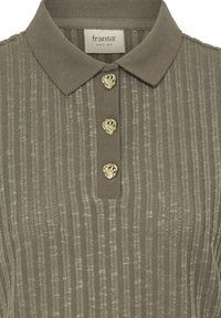 Polo kaki avec un design côtelé texturé, doté d'un col et de trois boutons dorés en forme de cœur au niveau du col.