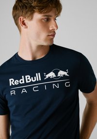 Marineblauwe T-shirt van katoen, met een groot wit "Red Bull Racing" logo en een grafisch ontwerp van een stier aan de voorkant.