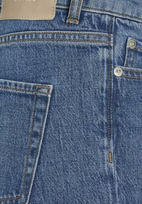 Mėlynos džinsinės kelnės su klasikinio penkių kišenių dizainu. Su matomu siuvimu ir odiniu ženkleliu ant juosmens. Lygi tekstūra.