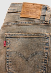 Πίσω τσέπη σε ξεθωριασμένο μπλε τζιν Levi's που δείχνει την κόκκινη ετικέτα Levi's και το καφέ δερμάτινο έμβλημα της μάρκας Levi Strauss & Co. στη μέση της ζώνης.