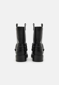 Botas de tobillo de cuero negras con un acabado suave, puntera redondeada, dobles tiradores y un tacón grueso. Incluye un detalle de correa ajustable.