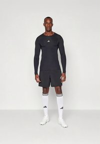 Svart langermet treningsskjorte med hvit logo, kombinert med svarte shorts, hvite sokker med svarte striper og hvite sportssko.