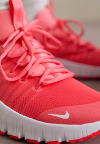 Pantofii sport Nike de culoare roz aprins, cu un material texturat pentru partea superioară, șireturi plate și talpă albă. Design minimalist, fără modele vizibile.