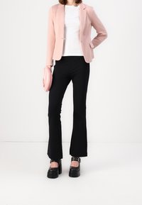 Light pink blazer over a white shirt, paired with black flared pants and chunky black platform shoes. The outfit includes a pink clutch.