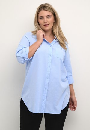Light blue, long-sleeve button-up shirt featuring a chest pocket, rounded hem, and rolled sleeves, made from a soft, textured fabric.