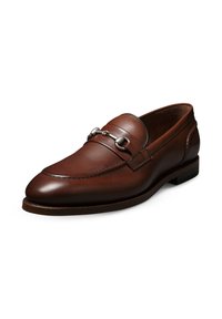 Mocassin en cuir marron avec un bout rond, des détails cousus et un accent en chaîne argentée sur le dessus. Talon bas empilé avec une texture lisse.