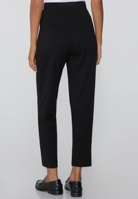Zwarte high-waisted broek met een rechtvallende pasvorm, voorzien van een gladde textuur, enkel-lange snit en zonder zichtbare patronen of accenten.
