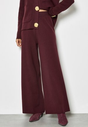 Pantalones de pierna ancha burdeos hechos de tela suave, con una cintura alta y un corte relajado. Combinados con botas de tacón moradas.