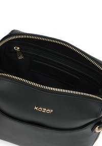 Fekete bőr kézitáska arany cipzárral és fémlemezekkel. Egyetlen fő rekesszel és egy belső cipzáras zsebbel rendelkezik. Arany színnel emblémázott logóval.