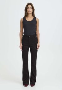 Top de tirantes negro acanalado combinado con jeans negros de cintura alta y acampanados. Ambas prendas tienen una textura suave y un diseño minimalista.