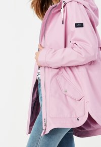 Jasnoróżowa wodoodporna kurtka z kapturem, z przodu na zamek, z elastycznym pasem i detalami w postaci bocznych kieszeni. Gładka faktura i casualowy design.