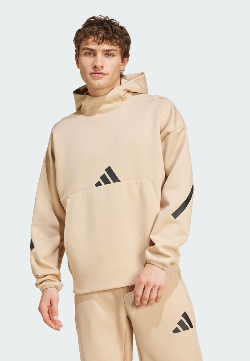 Hoodie beige con collo alto, caratterizzato da righe nere sulle maniche e un logo nero sul davanti. Realizzato in un tessuto morbido e testurizzato per garantire comfort.
