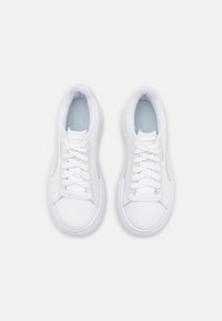 Un par de zapatillas deportivas blancas de caña baja con cordones, costuras visibles y plantillas de color azul claro, vistas desde arriba sobre un fondo blanco liso.