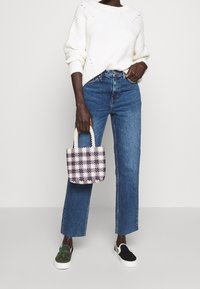 Vit, stickad tröja; blå, raka jeans; liten, rutig väska i lila och vitt med pärlhandtag; slip-ons i svart och kamouflage.