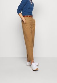 Tan high-waisted trousers with a straight-leg design, paired with a blue knit sweater and white sneakers with tan accents. Brown leather belt.