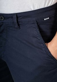 Navy blue chinos made of cotton blend, featuring a flat front, side pockets, and a button closure with a small brand tag near the waistband.