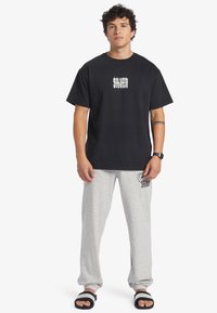 Black t-shirt with white graphic design, paired with gray sweatpants featuring a small black print. Worn with black sandals.